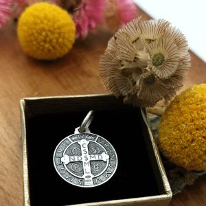 medalla con cruz griega con las inscripciones cssml y ndsmd en la cruz y otras letras alrededor y guardada en una caja y la caja rodeada de flores